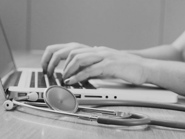 Händer skriver på laptop med stetoskop i förgrunden